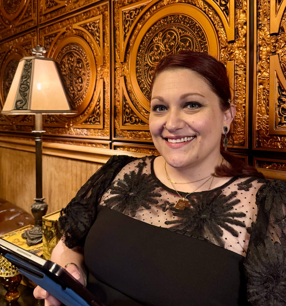 Rachel smiling while holding a tablet and wearing a black dress